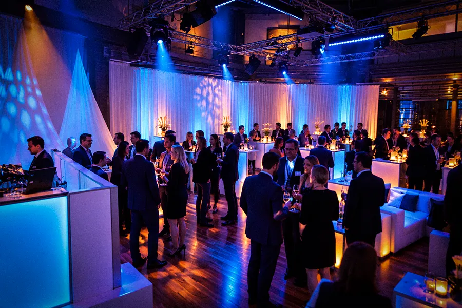 Gäste beim Get-together und Networking im OKTOGON auf Zollverein in Essen mit beleuchteten Stehtischen, Lounge-Möbeln und blau-violetter Eventbeleuchtung