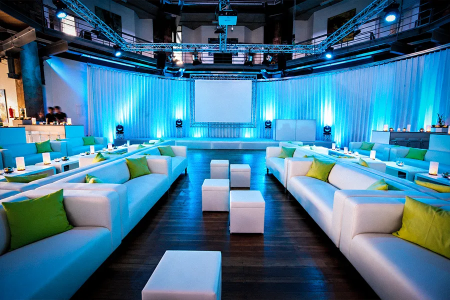 Lounge-Setup mit weißen Sofas, grünen Kissen und blauer Ambientebeleuchtung für Get-together und Networking im OKTOGON auf Zollverein in Essen