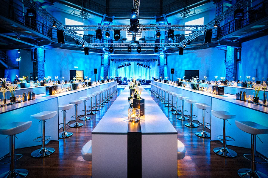 Hightable-Setup mit langen weißen Stehtischen, Barhockern und blauer Ambientebeleuchtung für Get-together und Networking im OKTOGON auf Zollverein in Essen
